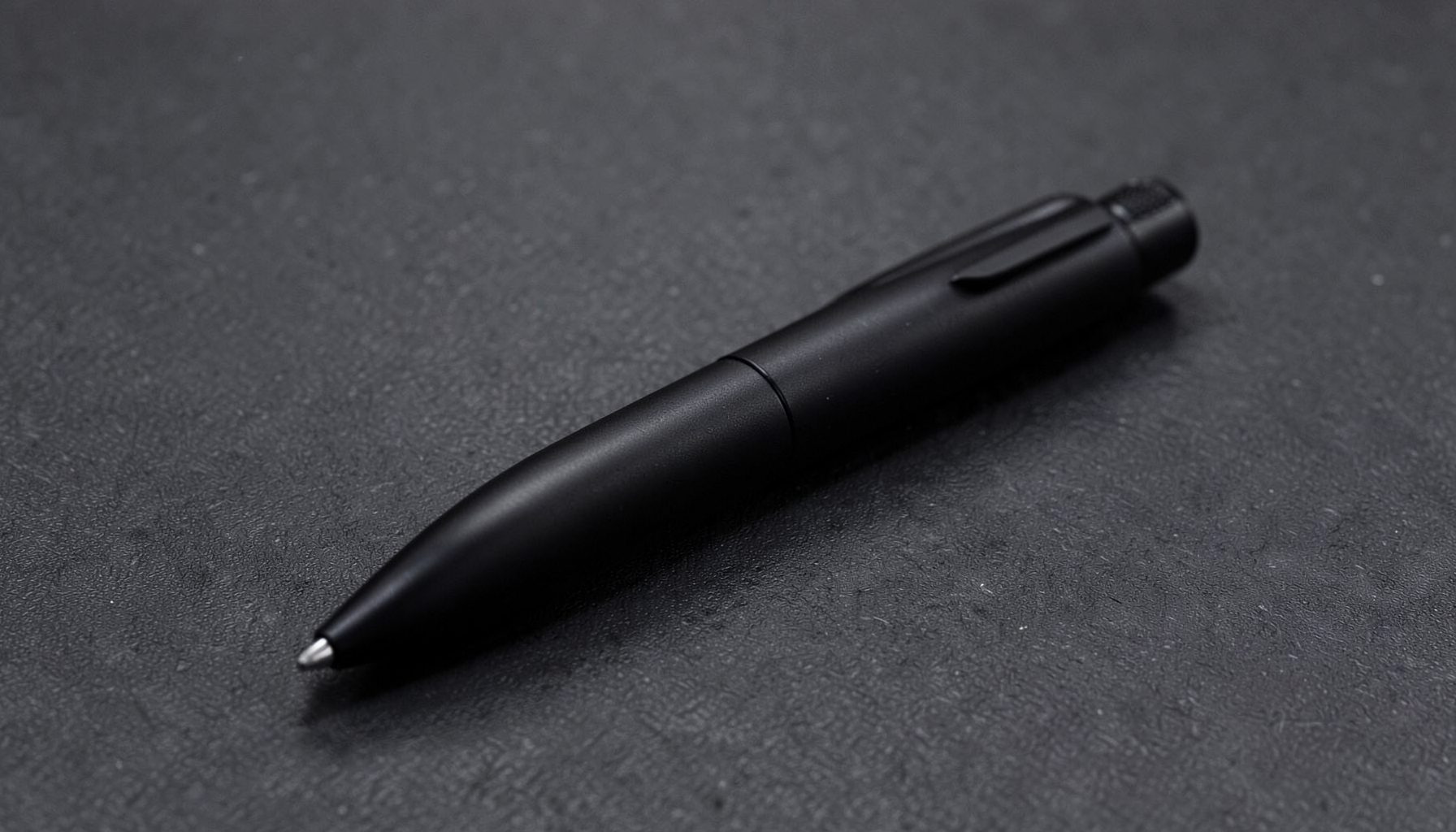 A black tactical pen on a dark textured surface, sleek and minimal