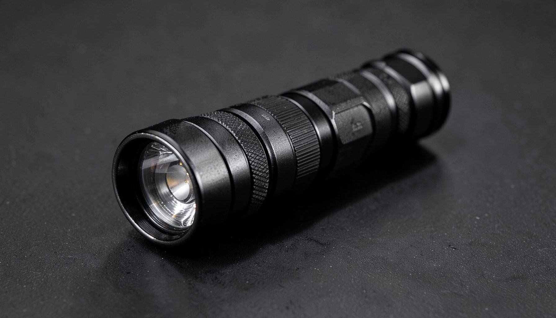 A rugged tactical flashlight on a dark surface, black and metallic silver tones