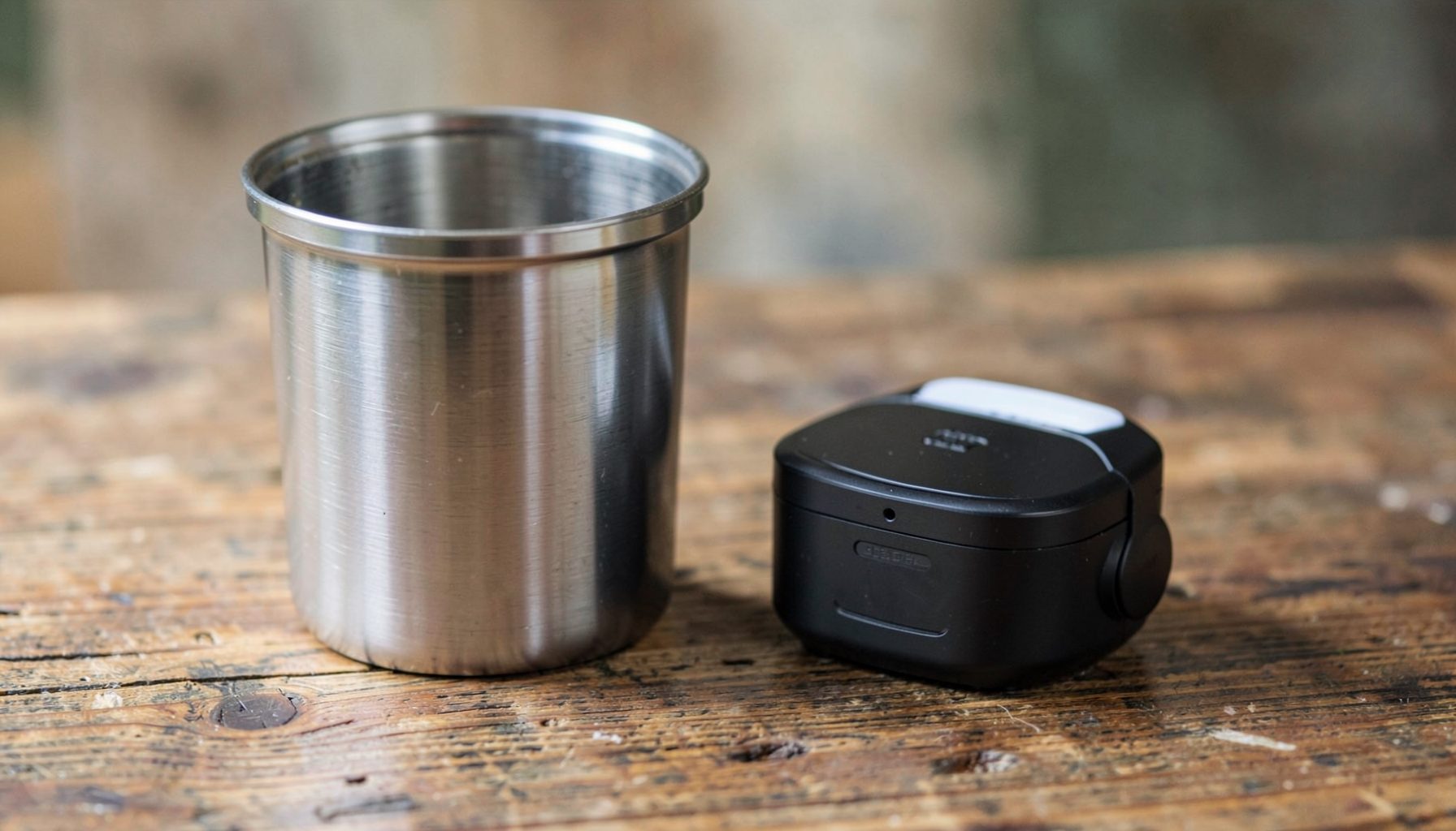 A stainless steel water container beside a small portable device on a rustic wooden table